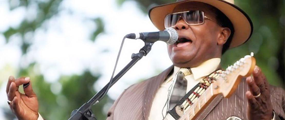 Norman Sylvester, 74, performing on stage and singing into a microphone.