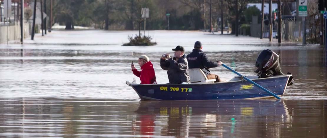 People taking photos from a small motorboat in the middle of a flooded street in Portland, Oregon.