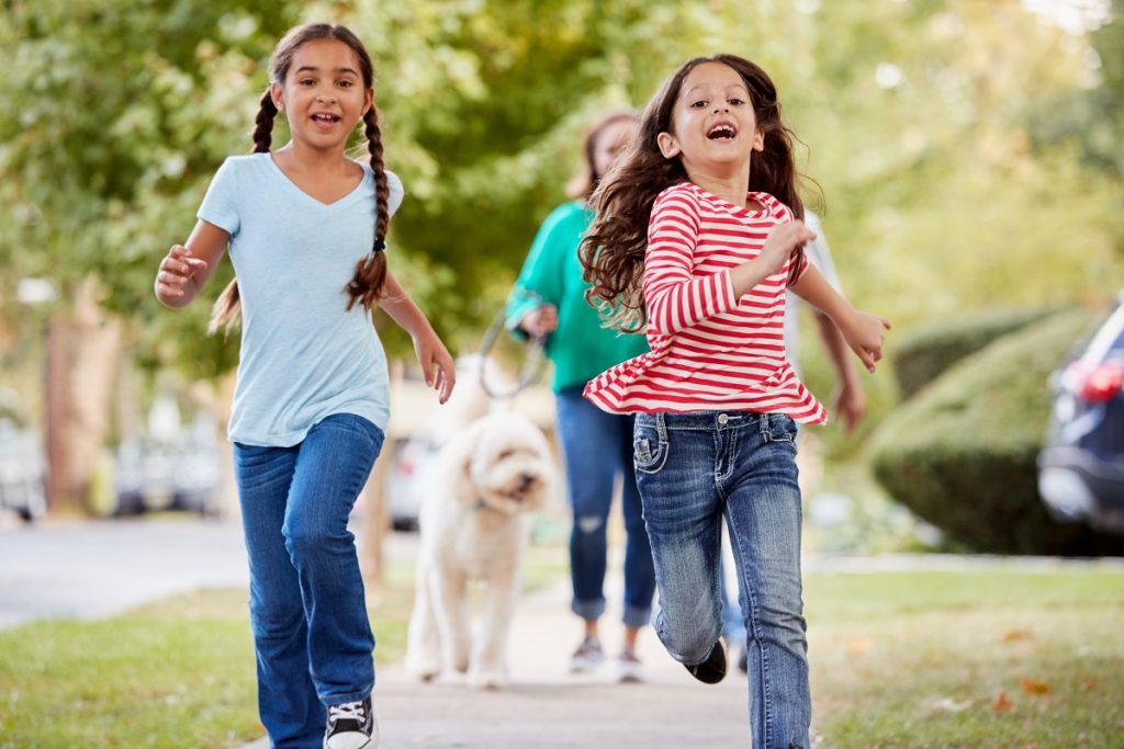 Young girls running along neighborhood sidewalk