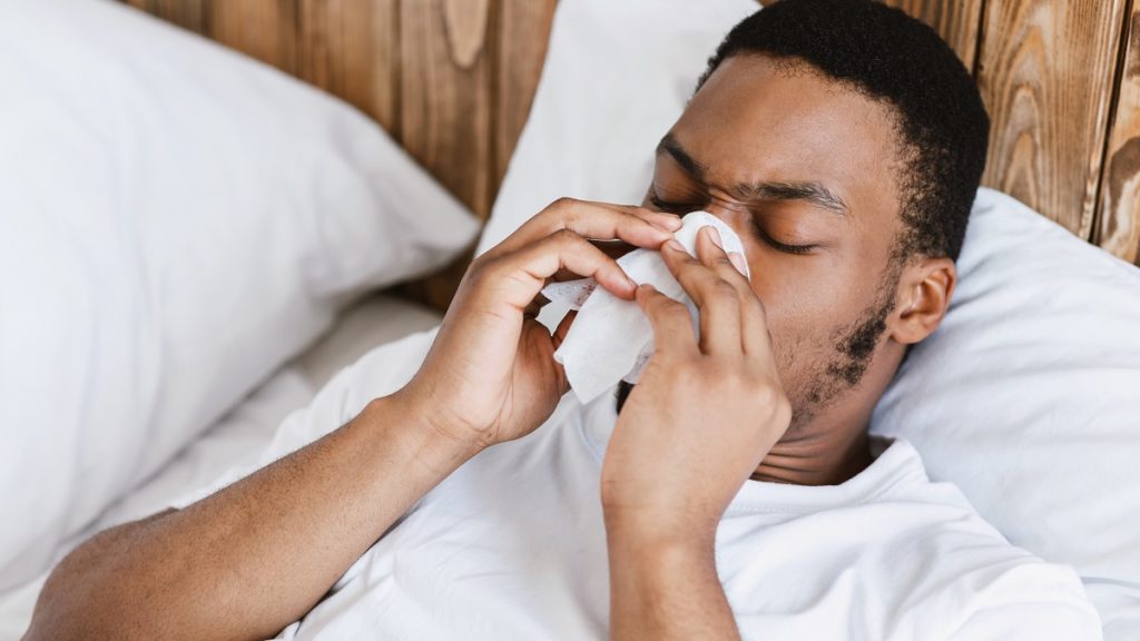 Man blowing his nose in bed