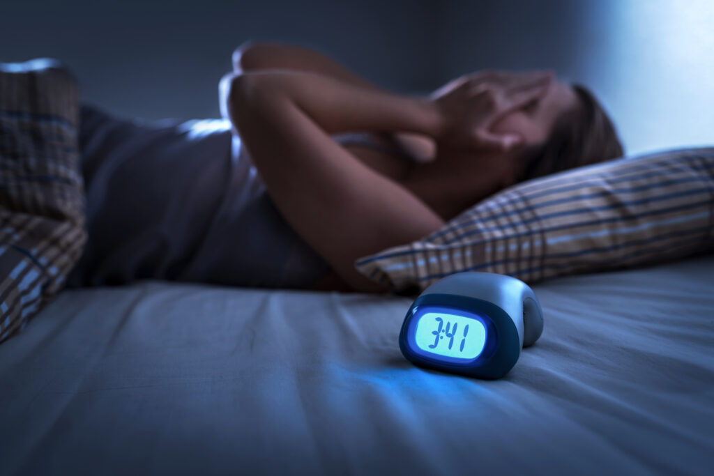 Woman lying in bed trying to sleep with digital alarm clock showing 3:41 a.m.