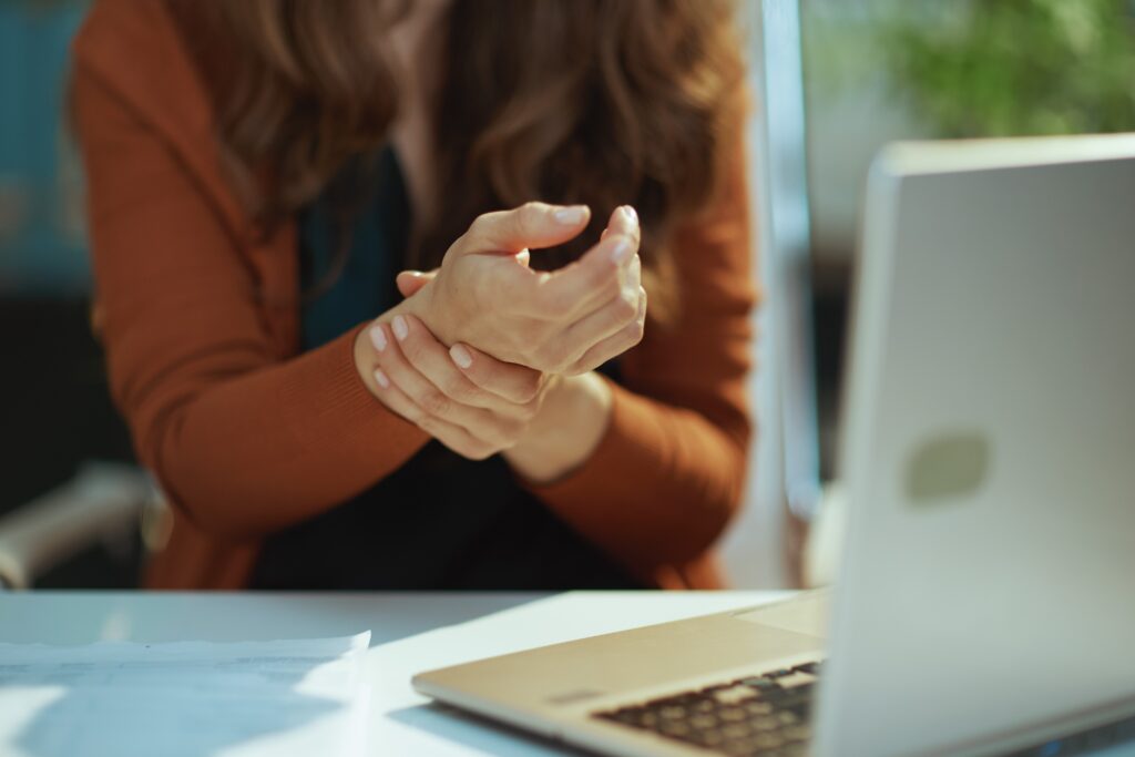 Woman sitting at a table with laptop open, holding her right wrist with her left hand