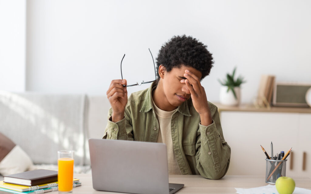 Young Black man sitting at a table experiencing eyestrain