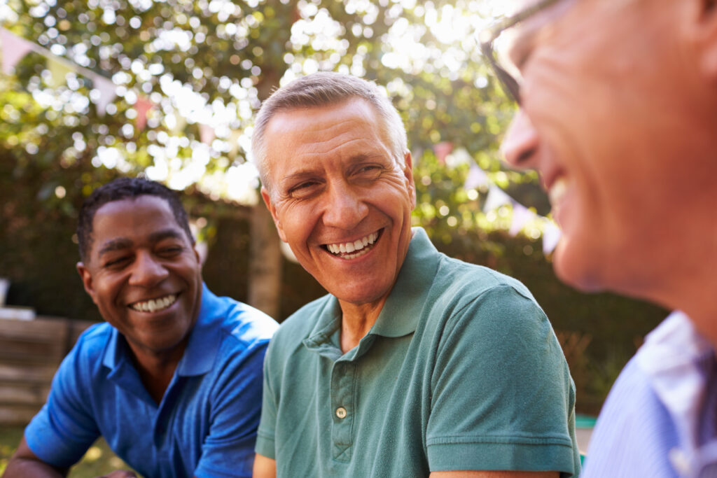 3 middle-aged male friends laughing in a backyard, discussing changes they experience in middle-age.