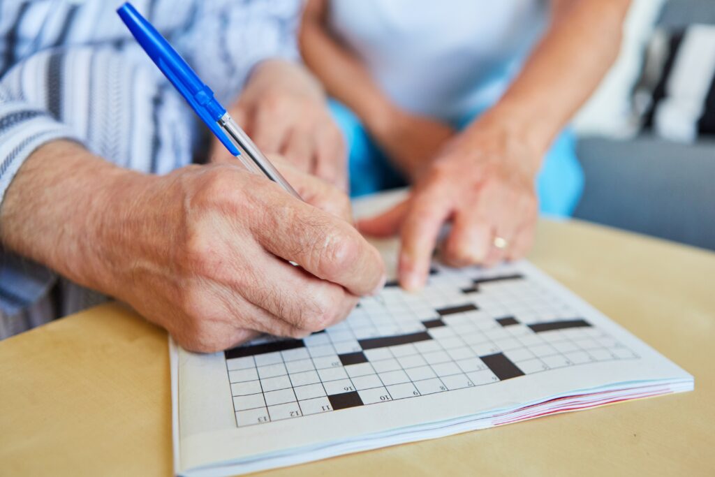 The hands of two seniors are shown as they fill out a crossword puzzle