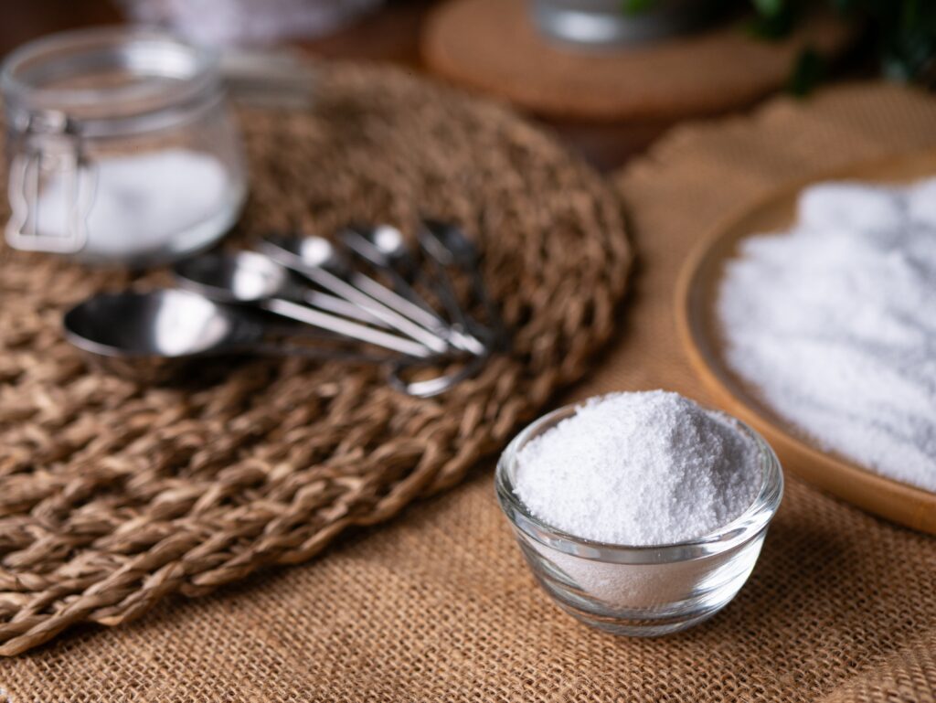 a bowl of sugar sits in the foreground with measuring spoons in the background