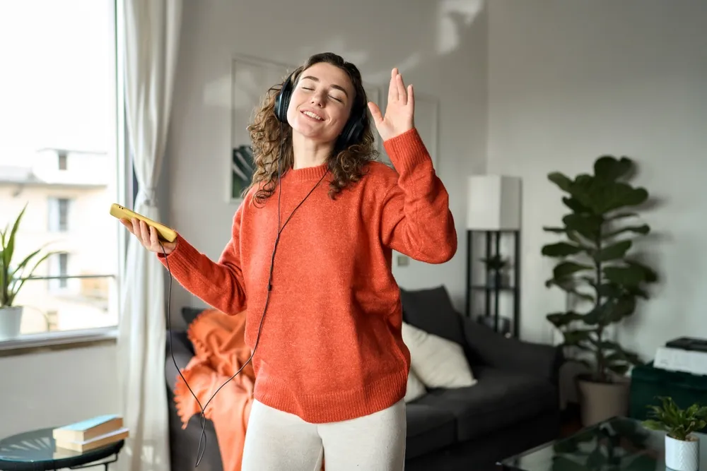 white woman with brown curly hair dances in a living room.